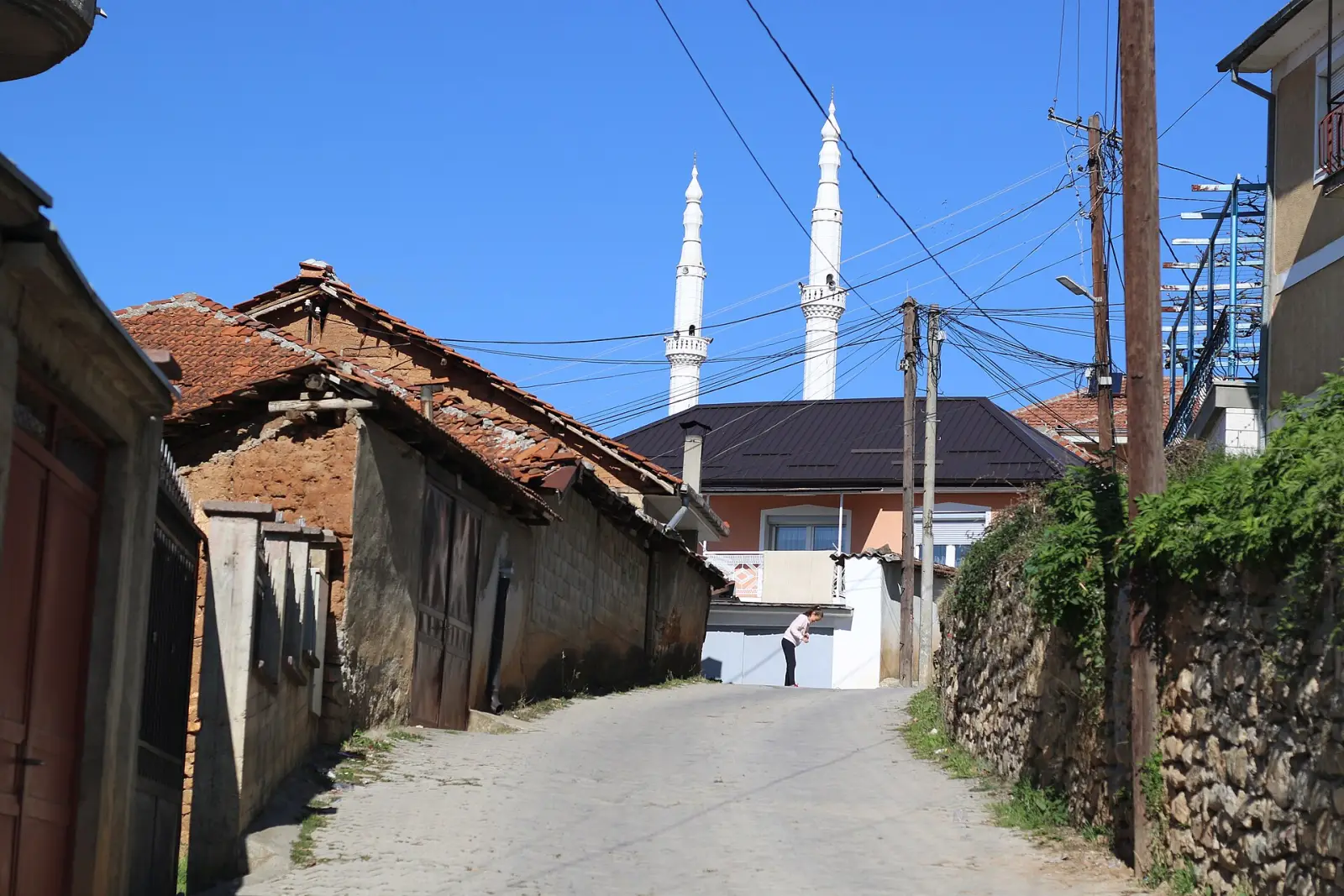 Тесна улица во старата чаршија на Дебар, со традиционални куќи и минарињата на џамијата во позадина