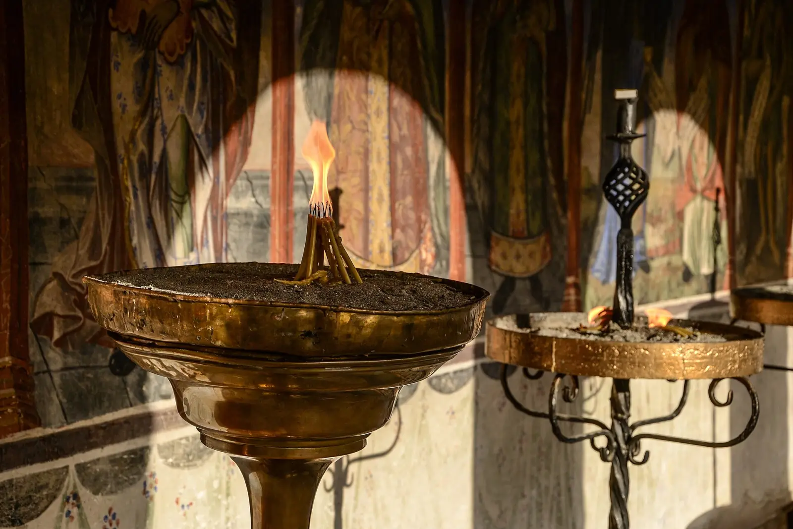 Кандило и свеќник пред живописните фрески во внатрешноста на манастирот Свети Јован Бигорски